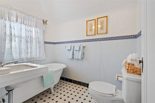 full bathroom featuring toilet, wallpapered walls, a soaking tub, and wainscoting