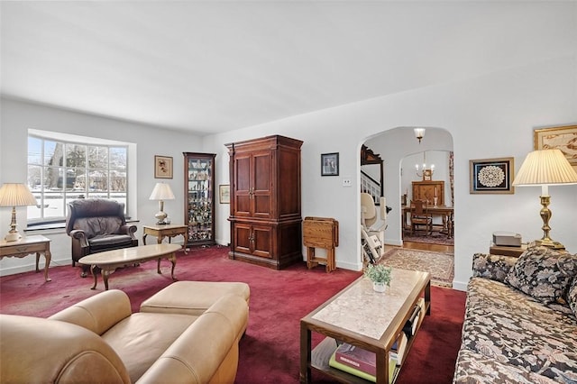 carpeted living area with arched walkways, stairway, baseboards, and a notable chandelier