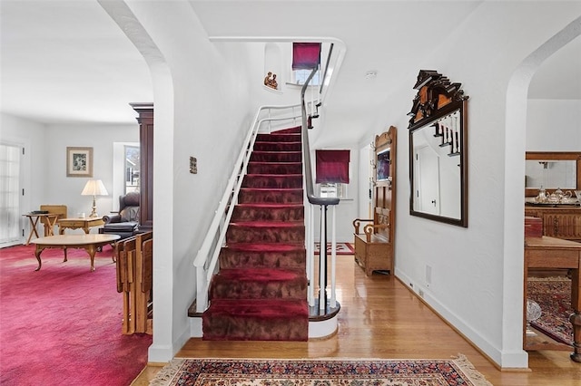 stairway with baseboards, arched walkways, and wood finished floors