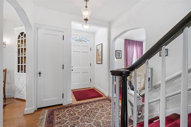 foyer entrance featuring light wood-style floors, baseboards, stairs, and arched walkways