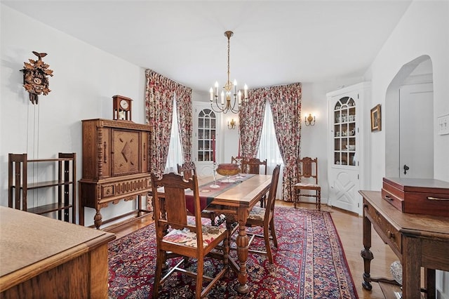 dining room with a chandelier, light wood finished floors, and arched walkways