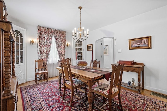 dining room with arched walkways, wood finished floors, visible vents, baseboards, and an inviting chandelier