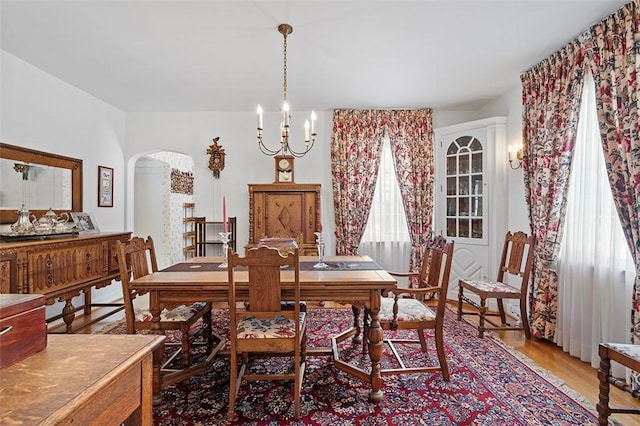 dining area featuring light wood-type flooring, arched walkways, and a chandelier