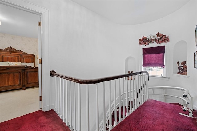 hallway with wallpapered walls, carpet flooring, and an upstairs landing