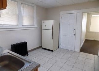 kitchen with a drop ceiling, a sink, freestanding refrigerator, and baseboards