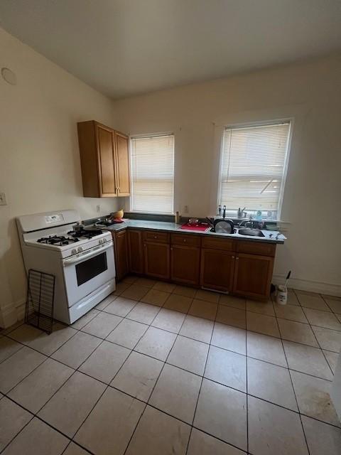 kitchen featuring baseboards, light tile patterned flooring, brown cabinets, and white gas stove