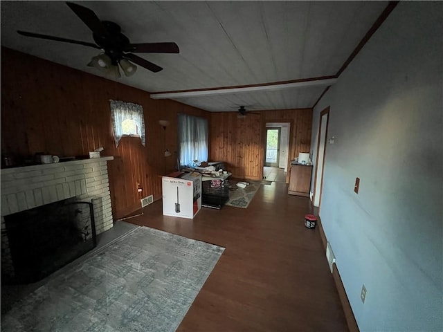 living area featuring wooden walls, visible vents, dark wood finished floors, ceiling fan, and a brick fireplace