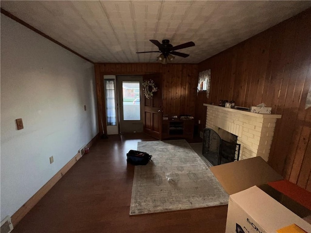 living area featuring a ceiling fan, a fireplace, wood walls, and baseboards