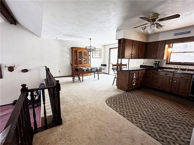 kitchen featuring carpet floors, dark countertops, a sink, dark brown cabinets, and ceiling fan with notable chandelier