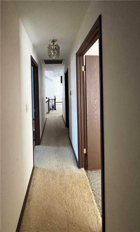 hall featuring light carpet, visible vents, an upstairs landing, and baseboards