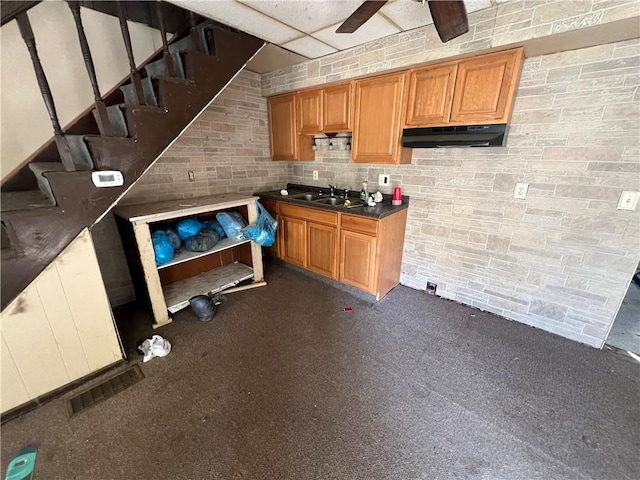 interior space with ceiling fan, under cabinet range hood, brick wall, a sink, and visible vents