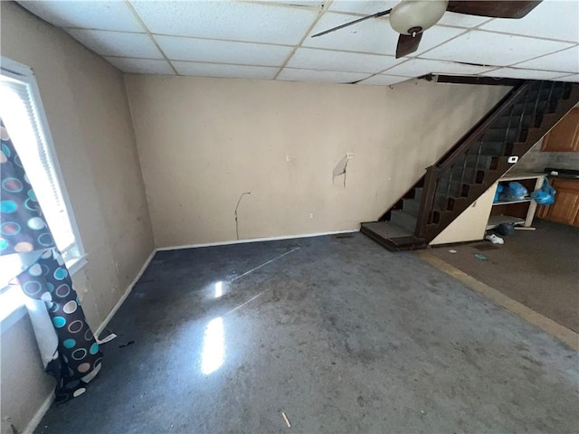 below grade area with a paneled ceiling, stairway, and baseboards