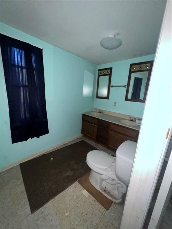 bathroom featuring baseboards, a sink, toilet, and double vanity