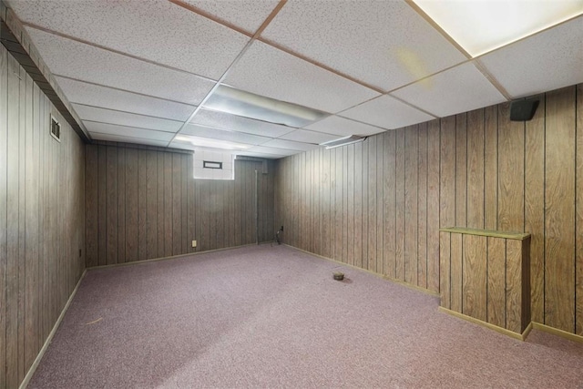 basement featuring carpet floors, visible vents, wood walls, and a drop ceiling