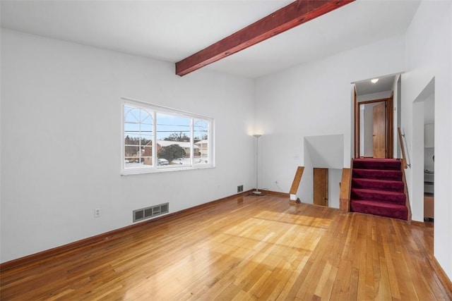 unfurnished living room featuring beam ceiling, stairway, wood finished floors, and visible vents