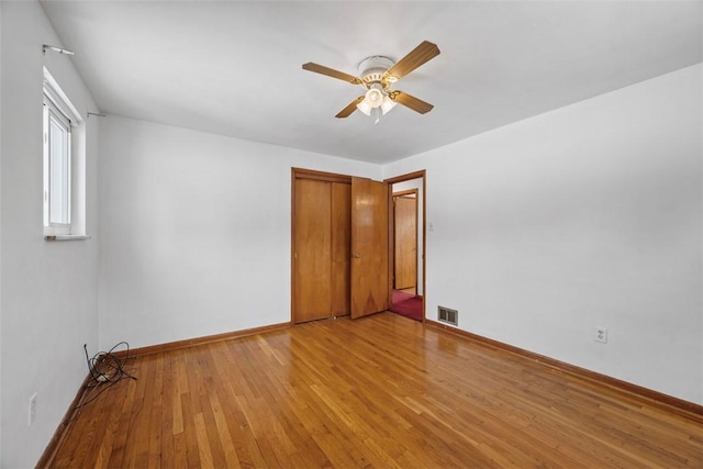 empty room with ceiling fan, light wood finished floors, visible vents, and baseboards