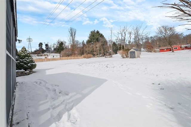 yard layered in snow featuring an outbuilding, a shed, and fence