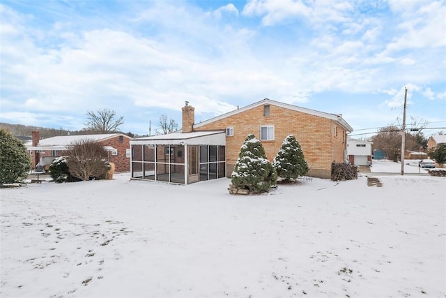 snow covered property with a sunroom, a chimney, and brick siding