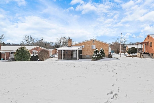 snow covered property featuring a chimney and a sunroom