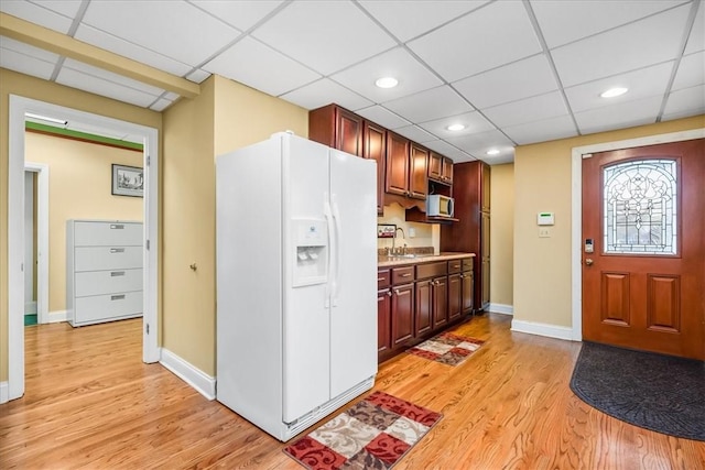 kitchen featuring light countertops, stainless steel microwave, light wood-style flooring, white fridge with ice dispenser, and baseboards