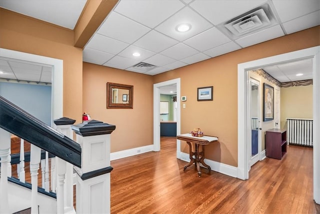 hall featuring a paneled ceiling, baseboards, visible vents, and wood finished floors