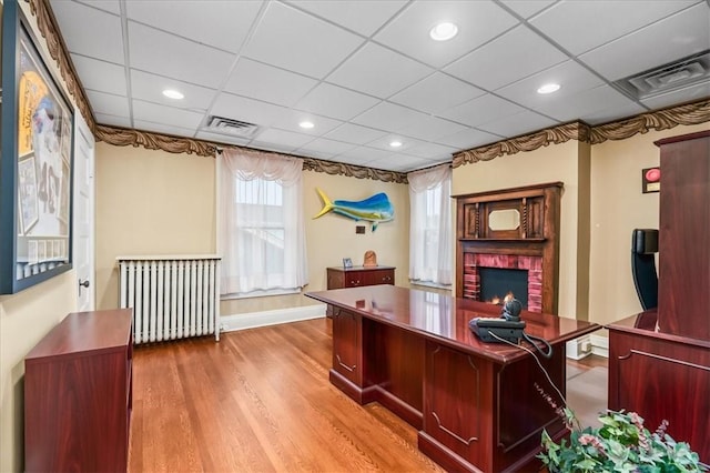 office area with light wood-style floors, a paneled ceiling, radiator, and visible vents