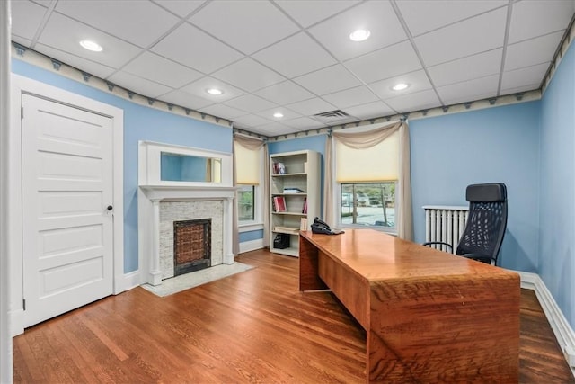 office featuring recessed lighting, wood finished floors, a fireplace with flush hearth, visible vents, and baseboards