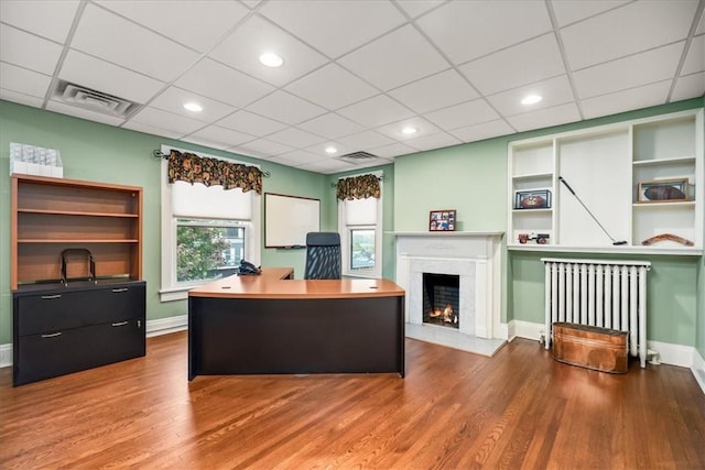 office space with visible vents, a lit fireplace, radiator heating unit, and wood finished floors