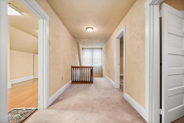 hall with light carpet, a textured wall, an upstairs landing, and baseboards