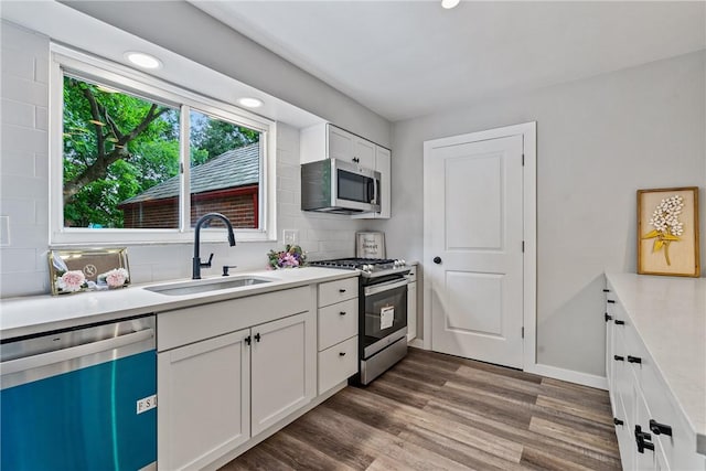 kitchen with dark wood finished floors, stainless steel appliances, light countertops, white cabinetry, and a sink