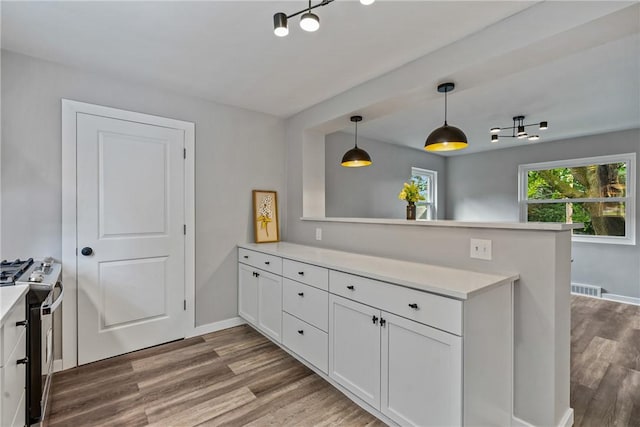 kitchen with stainless steel range with gas cooktop, white cabinets, light countertops, and a peninsula