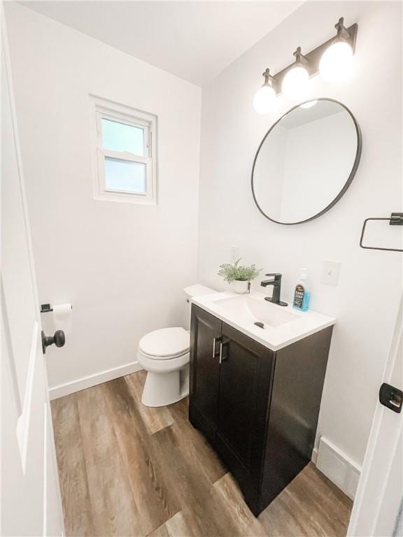 half bath with baseboards, vanity, toilet, and wood finished floors