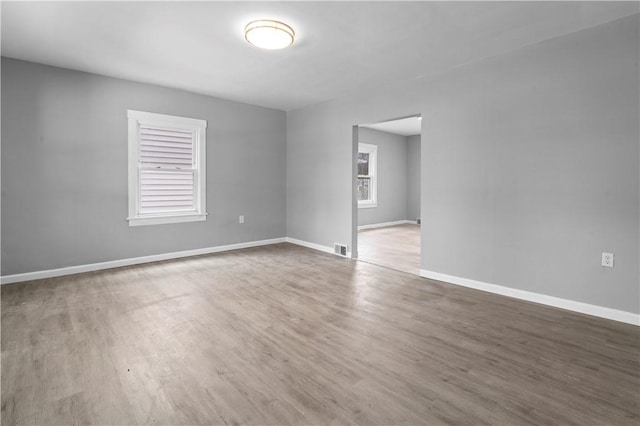 empty room featuring a healthy amount of sunlight, baseboards, visible vents, and wood finished floors