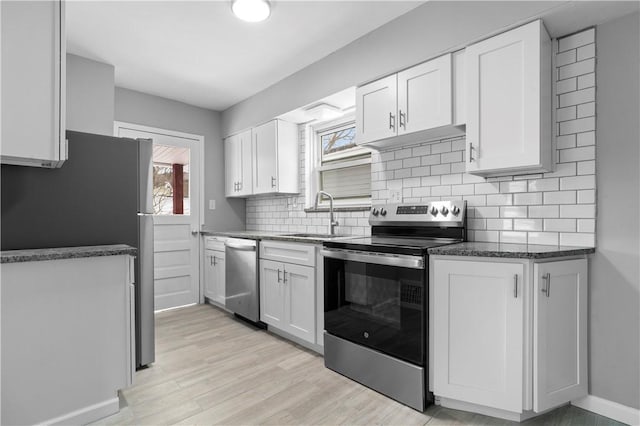 kitchen featuring stainless steel appliances, light wood-style flooring, decorative backsplash, white cabinetry, and a sink