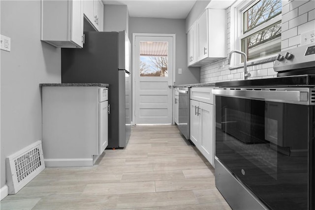 kitchen featuring visible vents, white cabinetry, appliances with stainless steel finishes, tasteful backsplash, and dark stone countertops