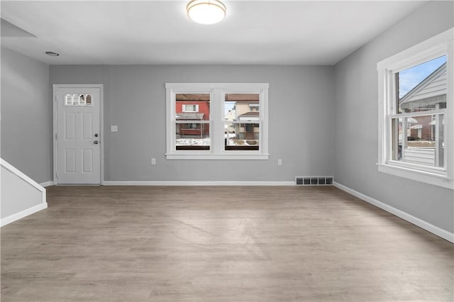 empty room with light wood-style flooring, visible vents, and baseboards