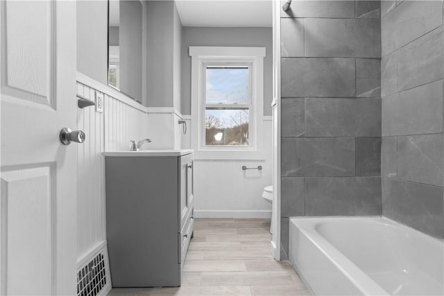 bathroom featuring visible vents, wainscoting, toilet, vanity, and washtub / shower combination