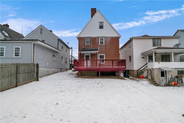 snow covered property with brick siding, a chimney, fence, and a wooden deck