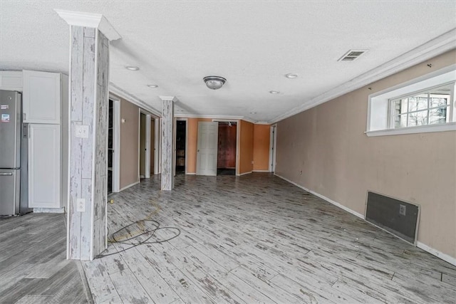 below grade area with ornamental molding, freestanding refrigerator, visible vents, and light wood finished floors