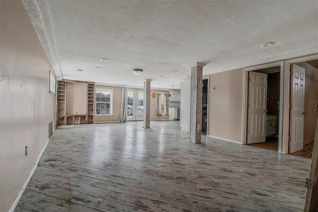 spare room featuring a textured ceiling, baseboards, wood finished floors, and ornate columns