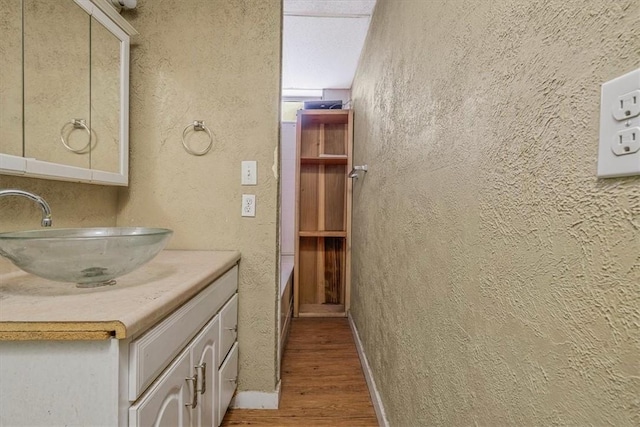 full bath featuring a textured wall, vanity, baseboards, and wood finished floors