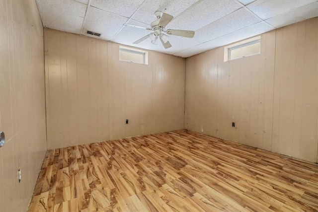 basement with a paneled ceiling, light wood-style flooring, visible vents, and ceiling fan