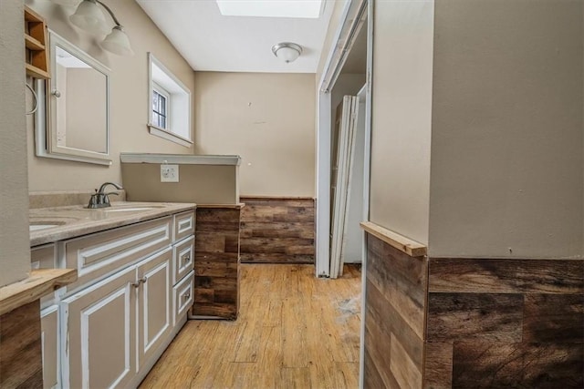 bathroom with a skylight, double vanity, a sink, and wood finished floors