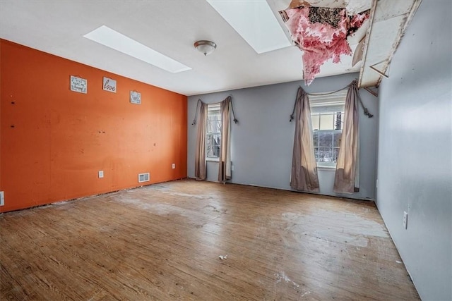 empty room featuring a skylight, plenty of natural light, wood finished floors, and visible vents