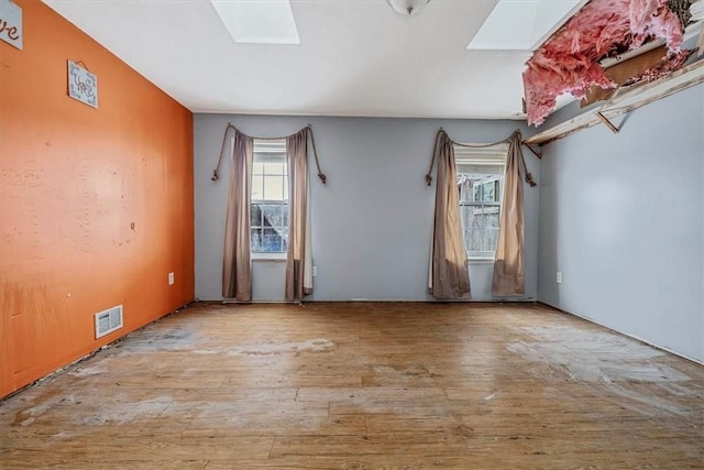 unfurnished room featuring light wood-type flooring, a skylight, and visible vents