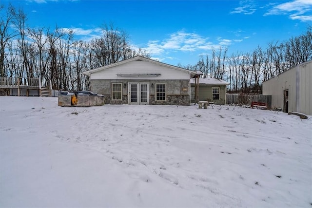 snow covered back of property with stone siding, a jacuzzi, french doors, and fence