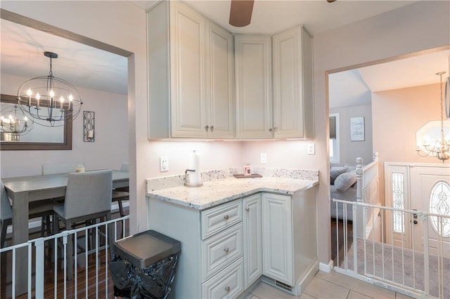 kitchen featuring pendant lighting, white cabinetry, light stone countertops, and a notable chandelier