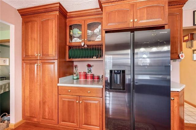 kitchen with brown cabinets, glass insert cabinets, stainless steel refrigerator with ice dispenser, and light countertops