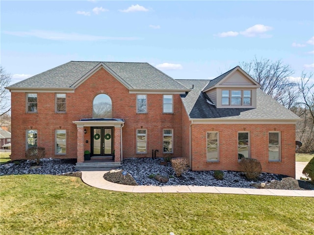 colonial-style house featuring a front lawn, french doors, brick siding, and a shingled roof