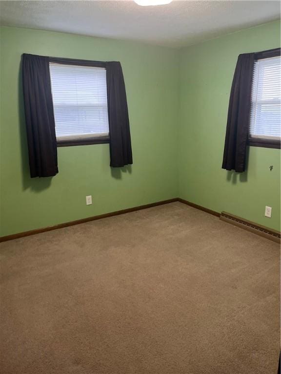 unfurnished room featuring a baseboard heating unit, light colored carpet, a textured ceiling, and baseboards